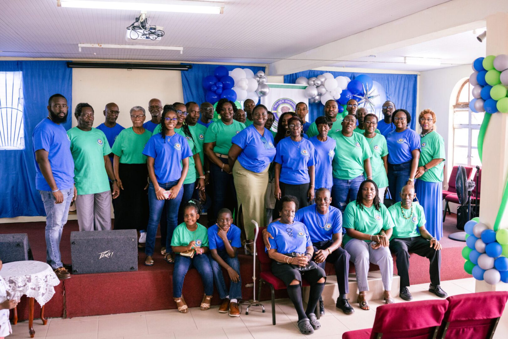 Group photo of people in matching blue and green shirts inside a room.