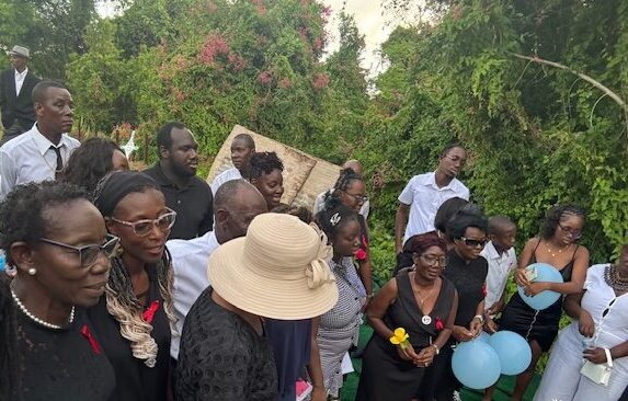 A group of people outdoors holding flowers and balloons in a peaceful gathering.