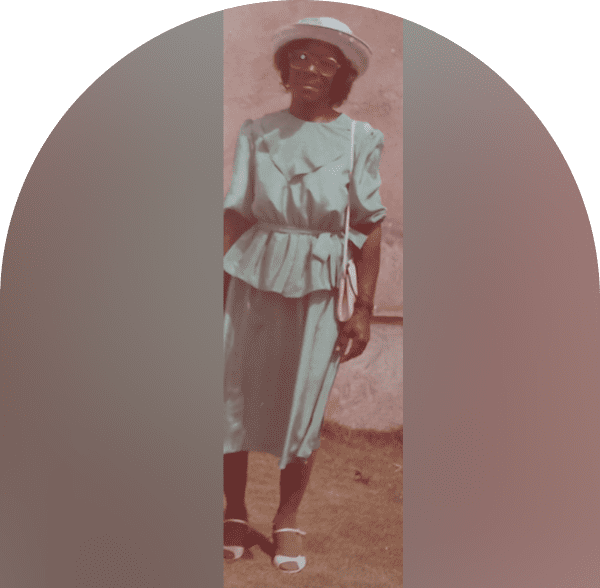 Woman in vintage attire posing outdoors with a hat and handbag.