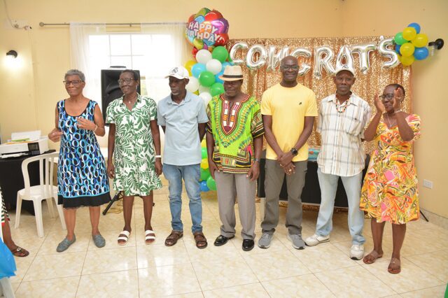Group of six people standing indoors with colorful balloons in the background.